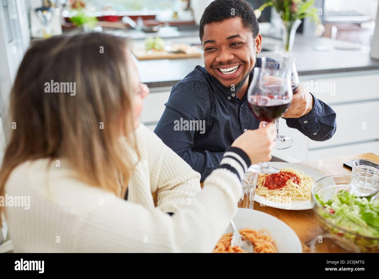Glückliche Freunde klirken Gläser Rotwein am Tisch, während sie zusammen Pasta essen Stockfoto