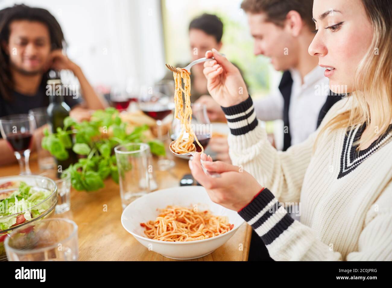 Frau, die mit Freunden am Esstisch Spaghetti mit Tomatensauce isst, während sie zusammen isst Stockfoto