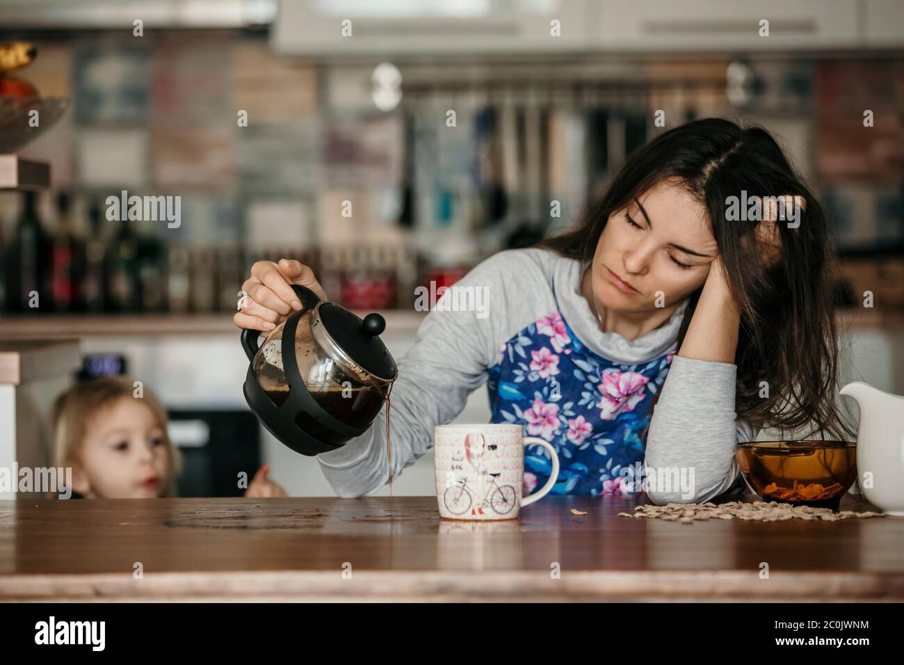 Müde Mutter, versuchen, Kaffee am Morgen zu gießen. Frau, die nach einer schlaflosen Nacht auf dem Küchentisch lag und versuchte, Kaffee zu trinken Stockfoto