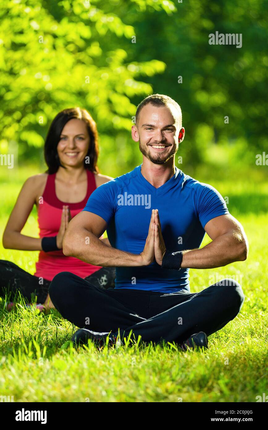 Junger Mann und Frau beim Yoga im sonnigen Sommerpark Stockfoto