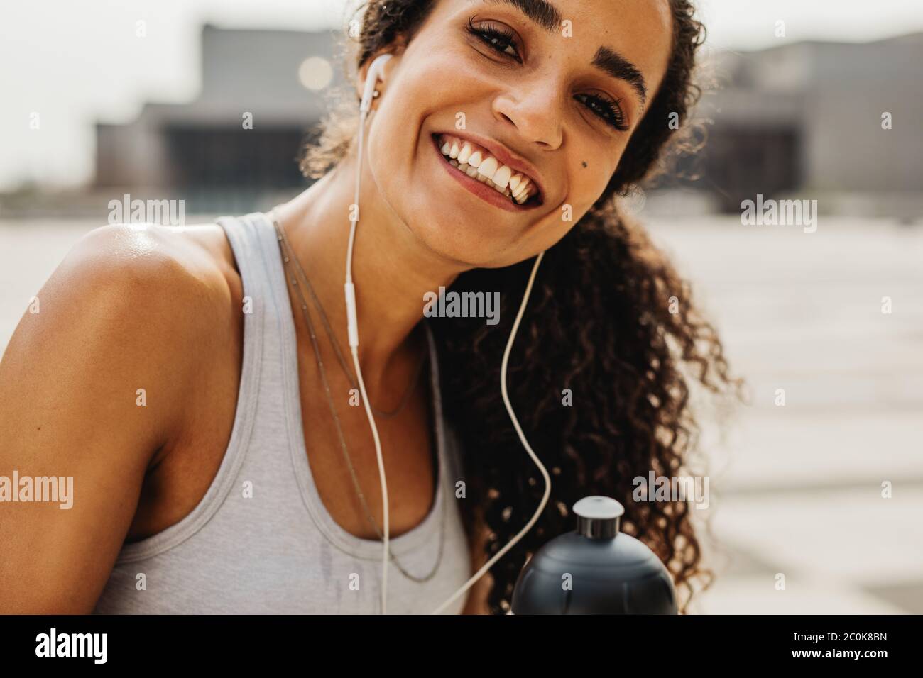 Lächelnde Fitness-Frau mit Ohrhörer, die auf die Kamera schaut. Weibliche Athletin, die morgens im Freien trainiert, Pause macht. Stockfoto