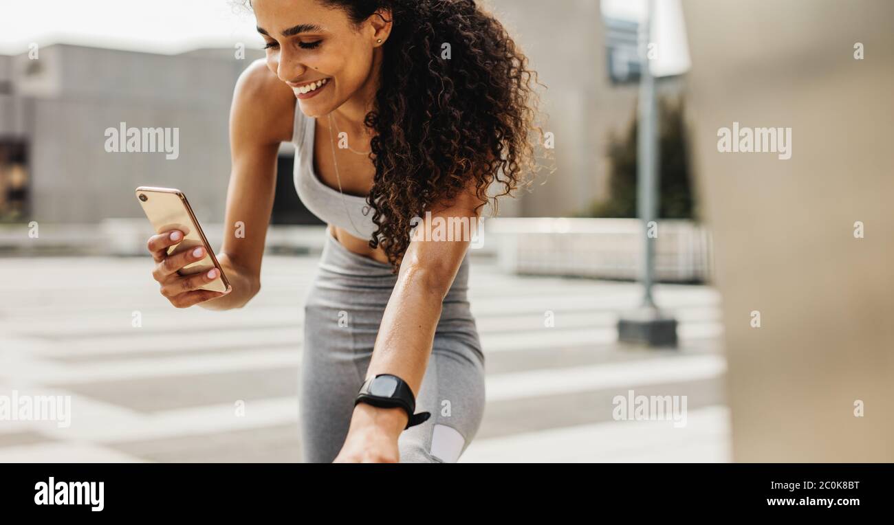 Fitness Frau mit Handy während des Trainings. Lächelnde Frau dabei Stretching-Training und mit ihrem Smartphone. Stockfoto