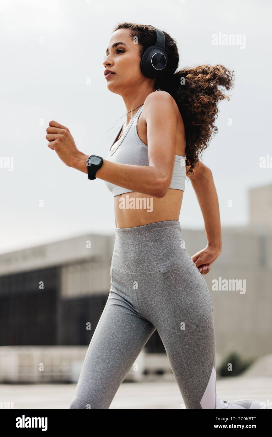 Athletische Frau, die durch die Stadt läuft. Frau in Sportkleidung und Kopfhörer tragen draußen in der Stadt laufen. Stockfoto