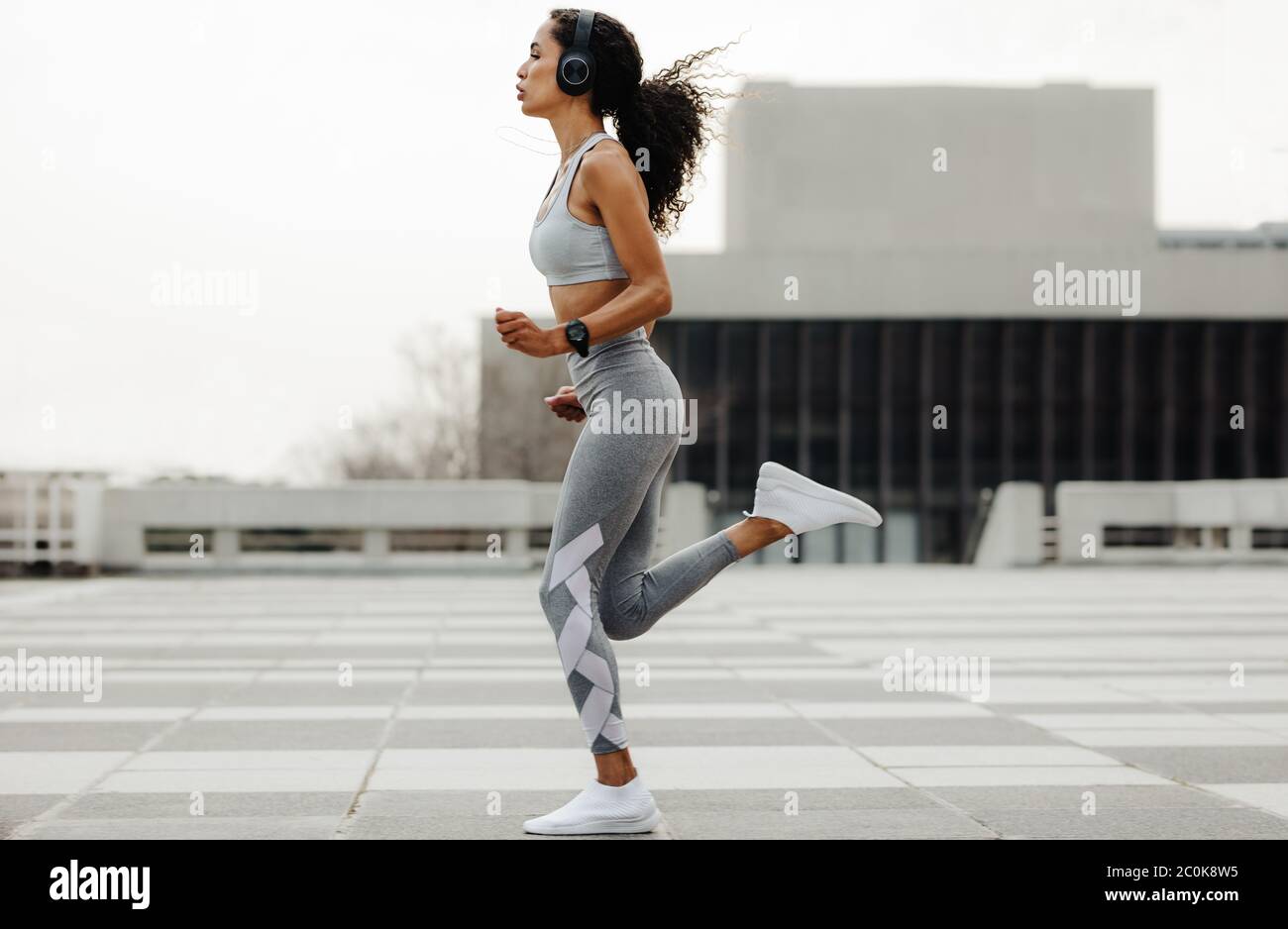 Ganzkörperaufnahme einer Fitness-Frau beim Joggen in der Stadt. Frau in Sportkleidung und Kopfhörer läuft im Freien. Stockfoto