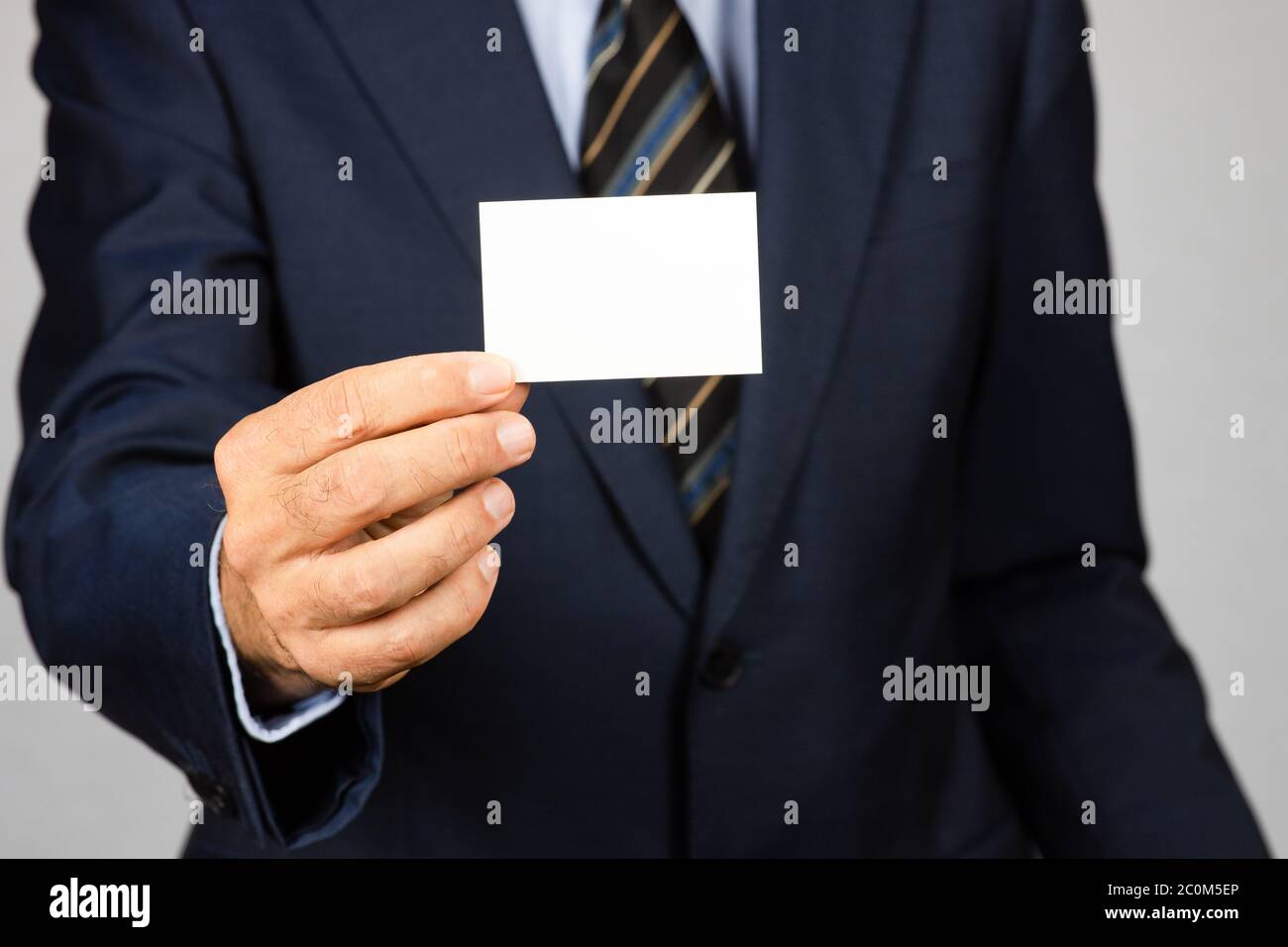 Geschäftsmann in Anzug mit einer leeren Visitenkarte vor sich. Selektiver Fokus auf den Vordergrund. Stockfoto