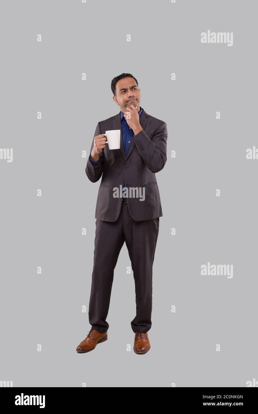 Geschäftsmann Denken Holding Coffee Cup. Indische Geschäftsmann stehend in voller Länge in Anzug mit Kaffee-Tasse Stockfoto