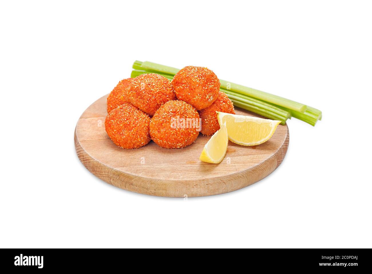 Rohe knusprige Hühnchen-Nuggets paniert in gemahlenem Chili-Pfeffer und Semmelbröseln auf einem Holzbrett mit Sellerie-Sticks und Zitrone. Bereit zum Braten. Frisch paniert Stockfoto