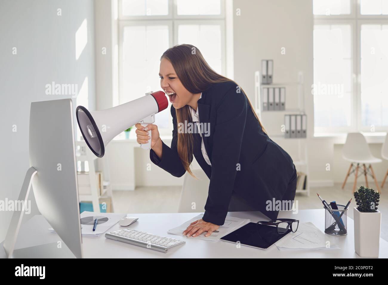 Unzufriedene Geschäftsfrau, die über Lautsprecher am Computer schreit Stockfoto