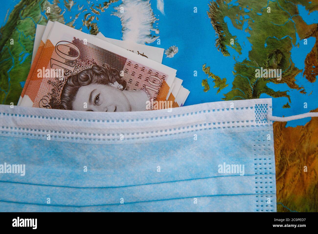 Globale Coronavirus-Pandemie und wirtschaftlicher Crash. Virus Facemask enthält britische Banknoten mit einem Hintergrund der Welt Stockfoto