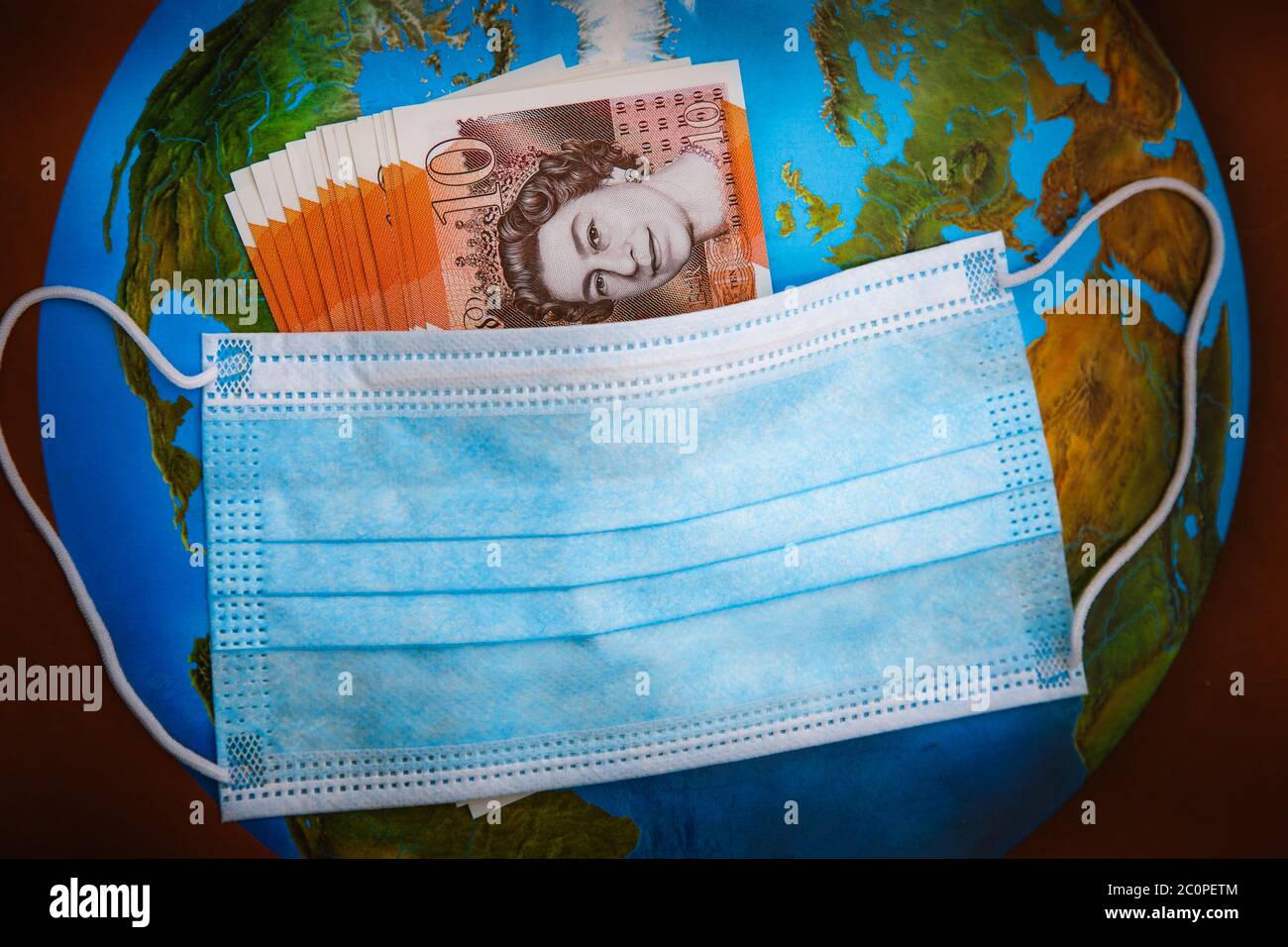 Globale Coronavirus-Pandemie und wirtschaftlicher Crash. Virus Facemask enthält britische Banknoten mit einem Hintergrund der Welt Stockfoto