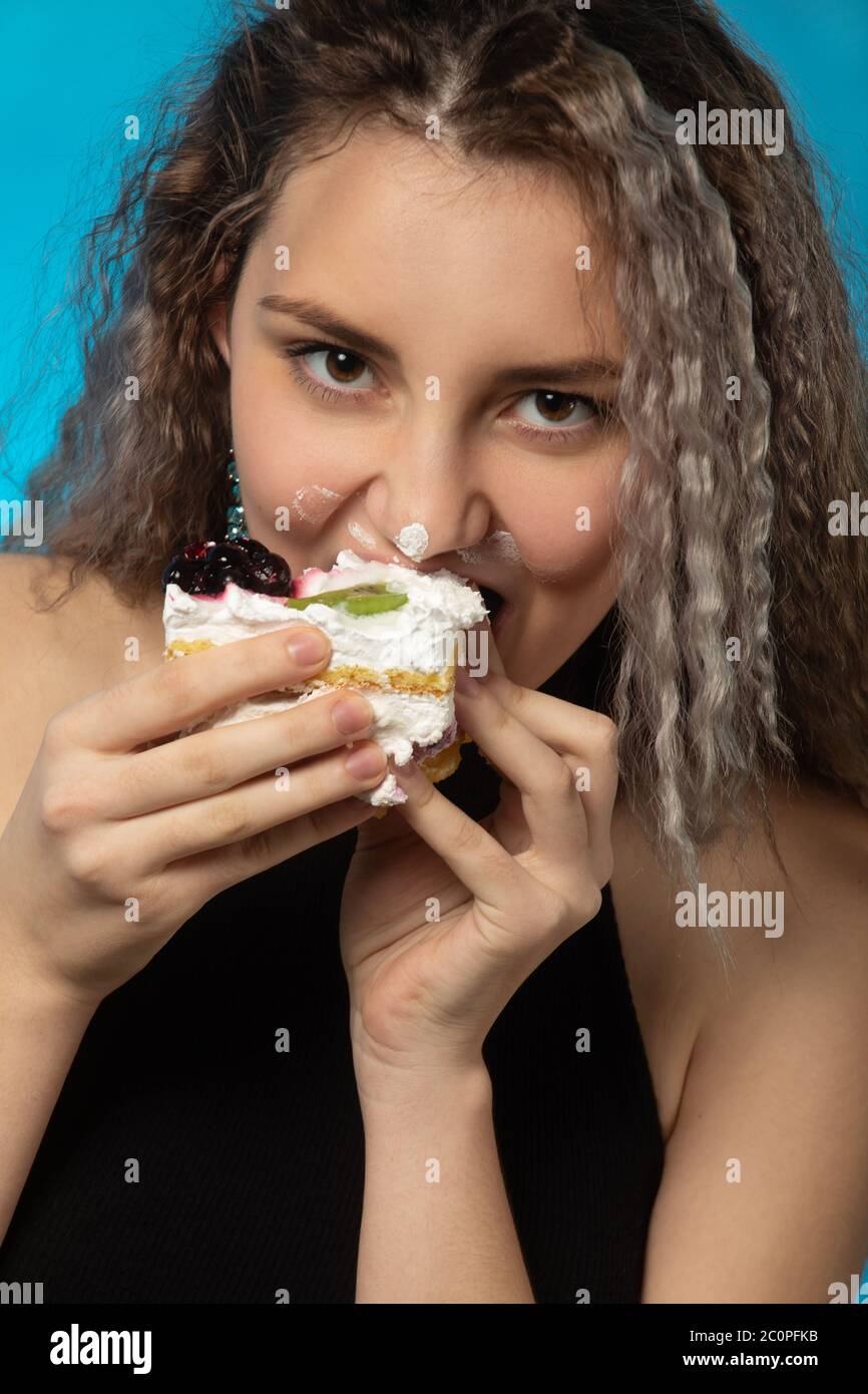 Lustige junge Frau mit Sahne auf dem Gesicht isst süßes Dessert, überessen macht Grimace Stockfoto