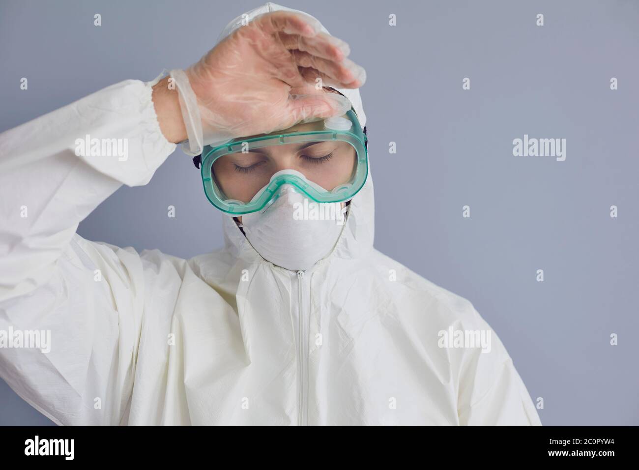 Müde Arzt trägt Hazmat Anzug auf grauem Hintergrund. Medizinischer Spezialist erschöpft von Infektionskrankheit Pandemie Stockfoto