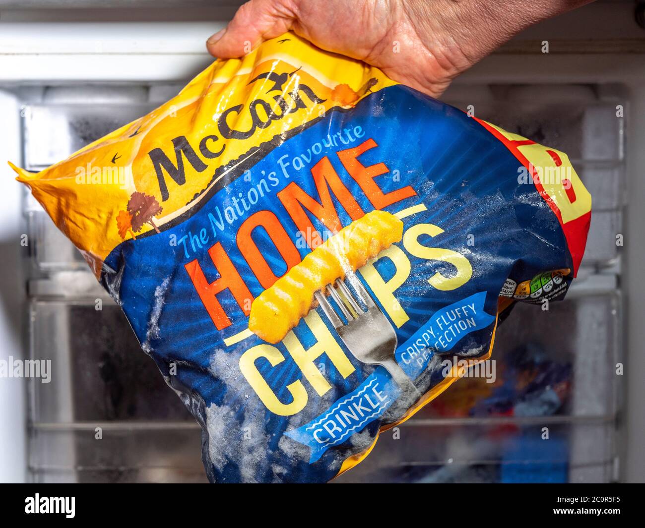 Ein Mann Hand hält eine Tasche von McCain crinkle geschnitten gefrorenen  Home Chips, vor einem Gefrierschrank Stockfotografie - Alamy