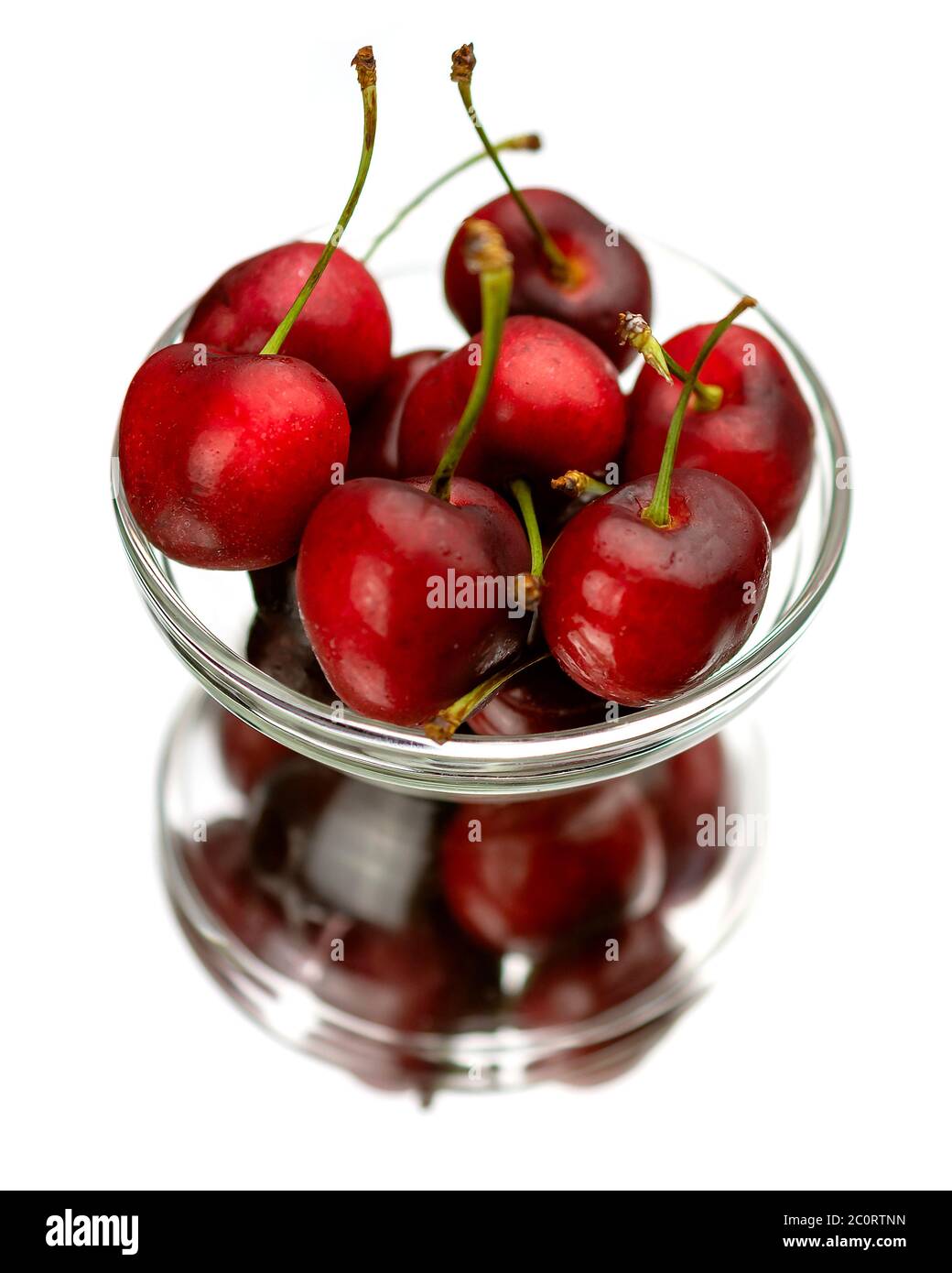 Eine klare Glasschale mit Kirschen auf einem Spiegel mit Reflexion. Weißer Hintergrund. Stockfoto