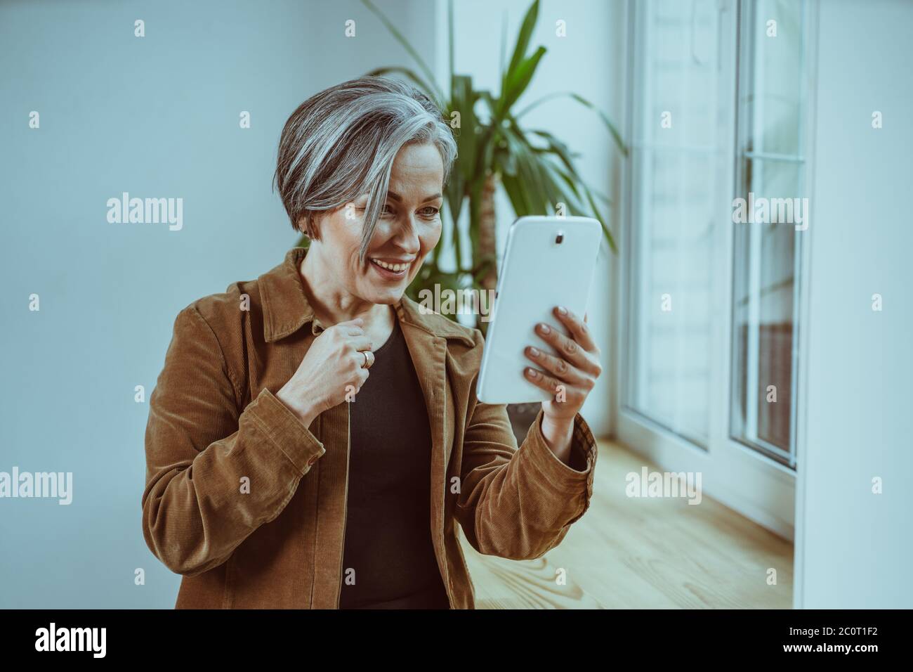 Fröhliche silberhaarige Frau kommuniziert online auf einem digitalen Tablet. Schöne reife Frau lächelt mit Online-Treffen mit ihren schönen Menschen bleiben Stockfoto