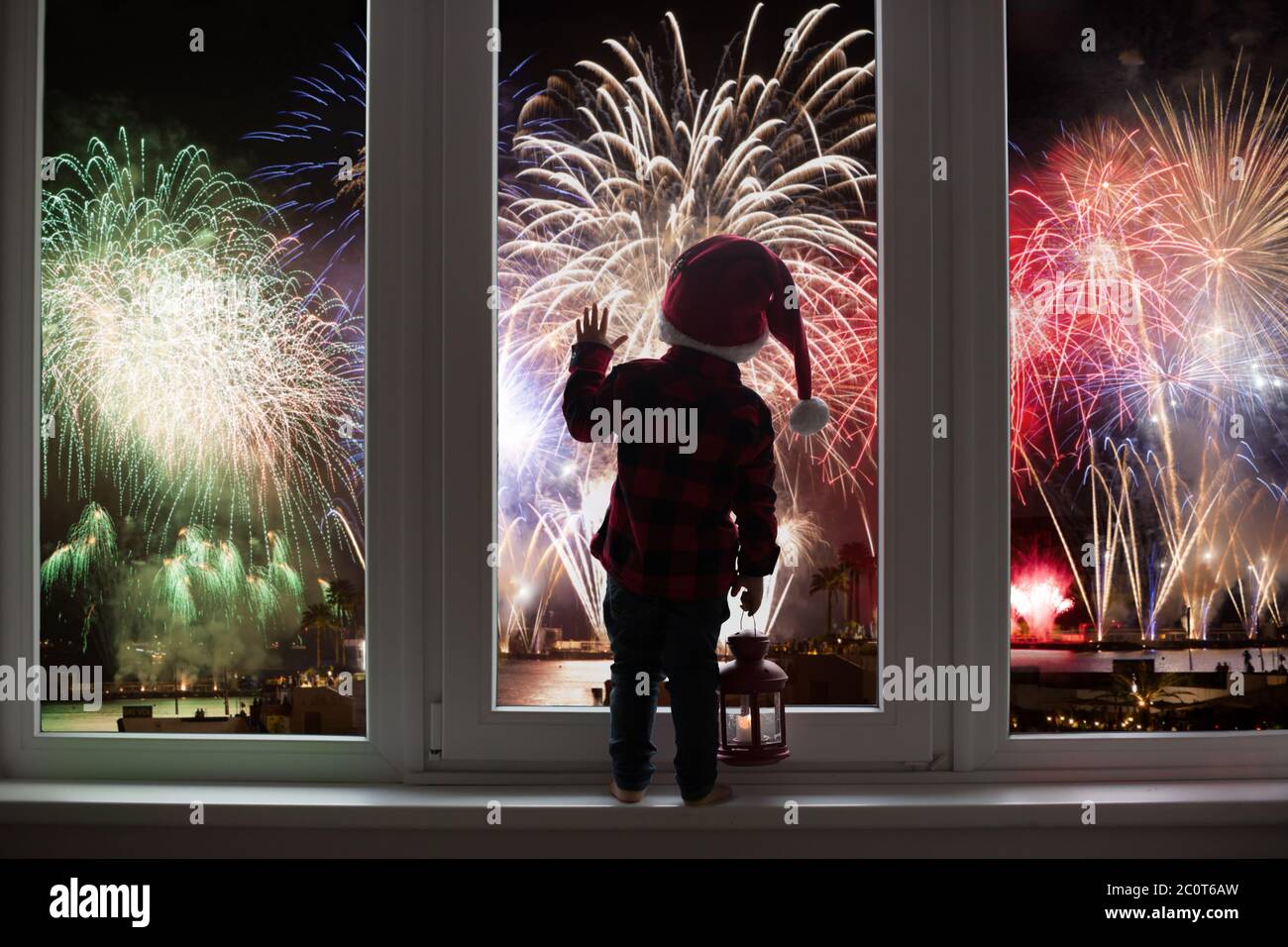 Kleinkind Kind vor einer großen französisch Türen stehend, lehnt sich an sie Blick auf Silvester Feuerwerk, mit Laterne Stockfoto