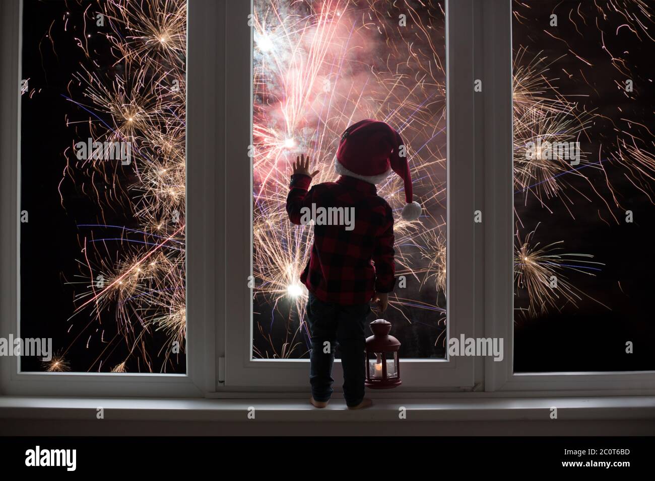 Kleinkind Kind vor einer großen französisch Türen stehend, lehnt sich an sie Blick auf Silvester Feuerwerk, mit Laterne Stockfoto