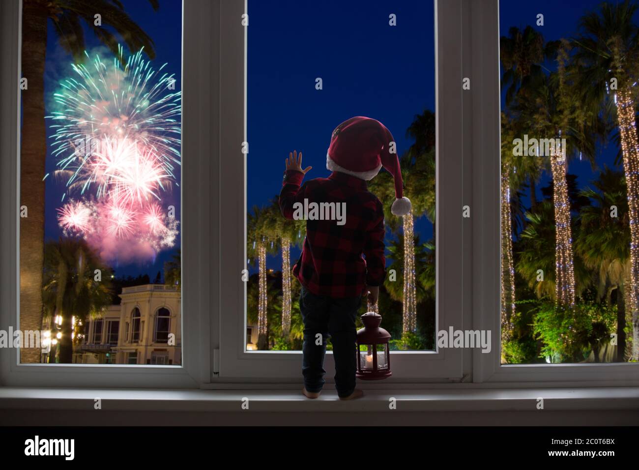 Kleinkind Kind vor einer großen französisch Türen stehend, lehnt sich an sie Blick auf Silvester Feuerwerk, mit Laterne Stockfoto