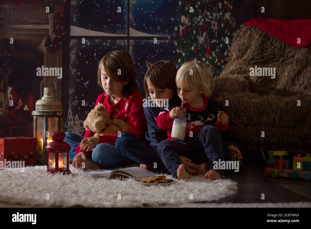 Drei Kinder, junge Brüder, lesen ein Buch in der Weihnachtsnacht in einem gemütlichen Zimmer auf Kerzen Stockfoto