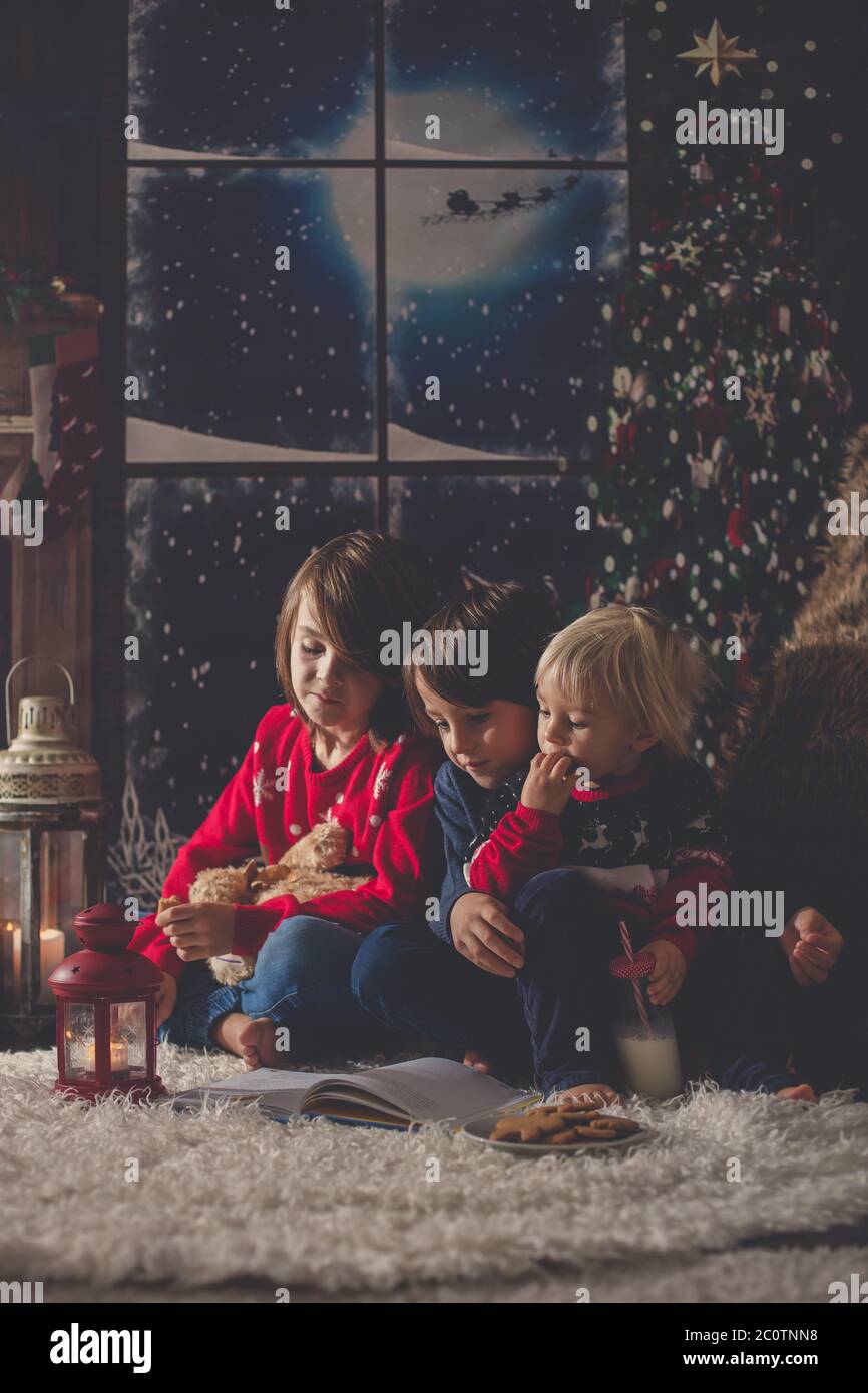 Drei Kinder, junge Brüder, lesen ein Buch in der Weihnachtsnacht in einem gemütlichen Zimmer auf Kerzen Stockfoto