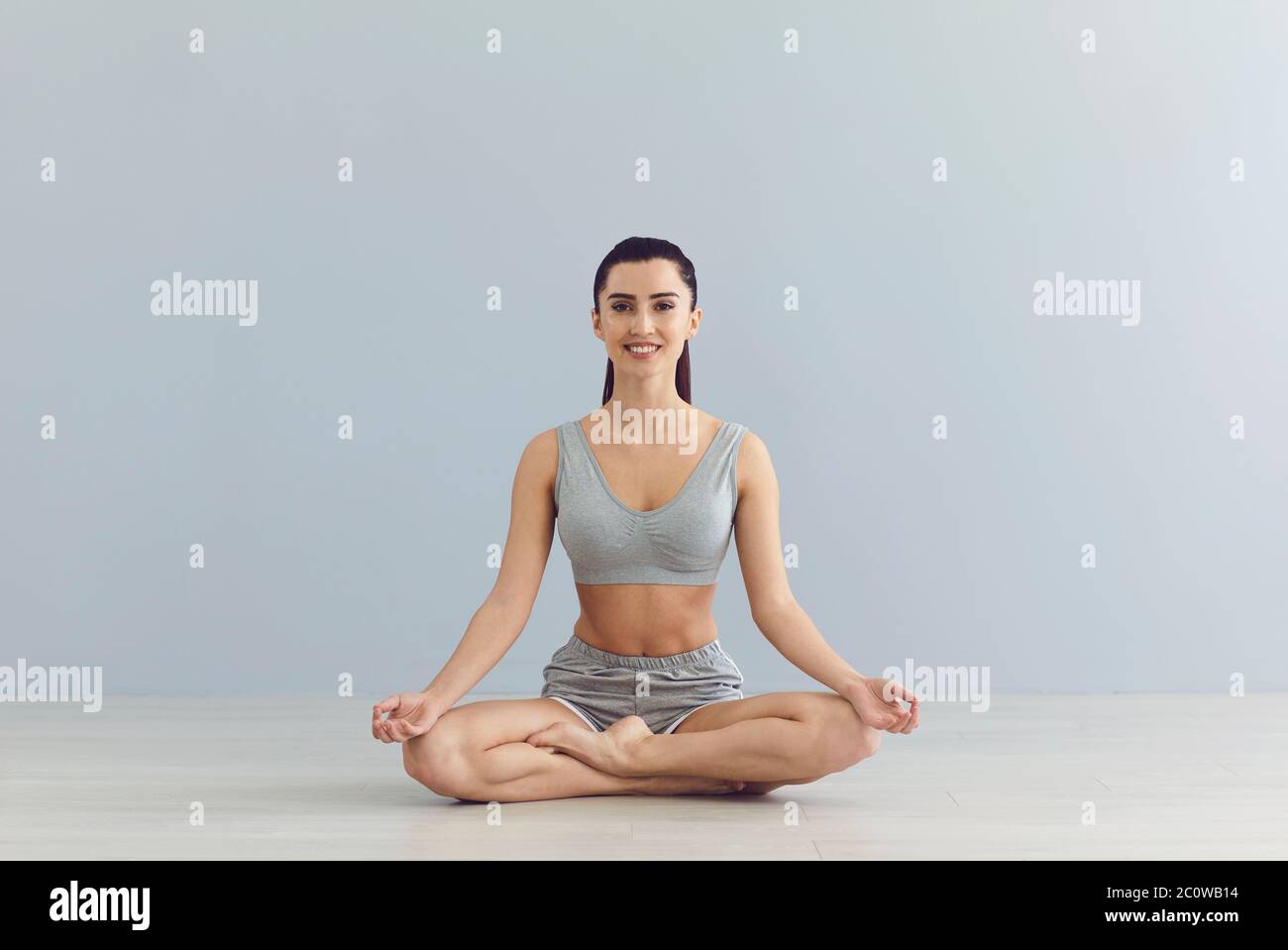 Yogalehrer sitzt in Lotuspose und schaut auf die Kamera auf grauem Hintergrund. Meditationslehrer in der Klasse im Studio Stockfoto