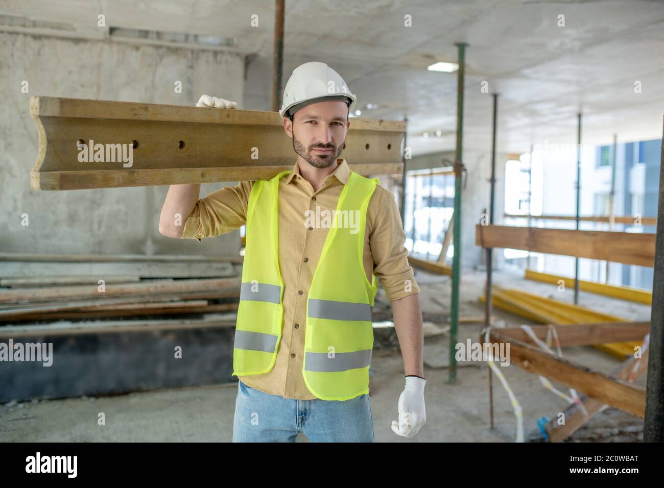 Bauarbeiter in gelber Weste und Handschuhe tragen Holzbrett auf der  Schulter Stockfotografie - Alamy