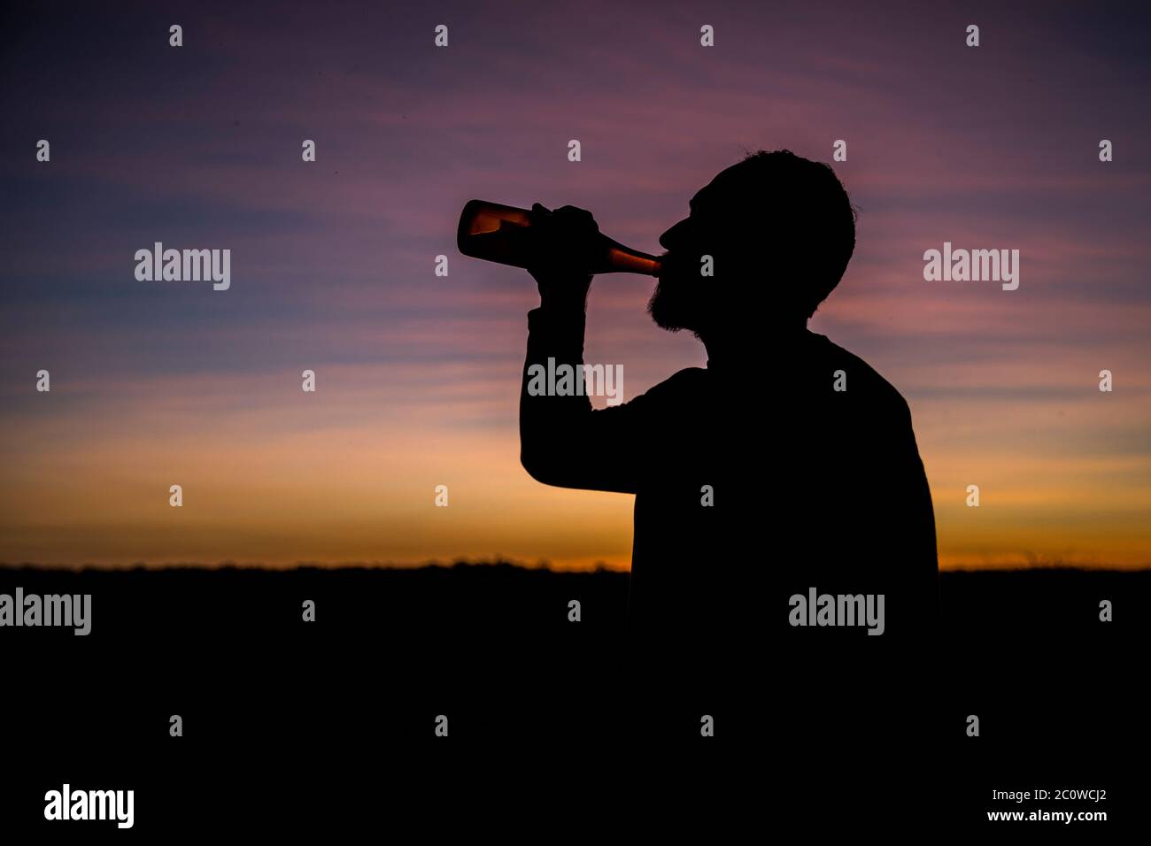 Mann trinkt Bier im Sonnenuntergang mit Rücklicht Stockfoto