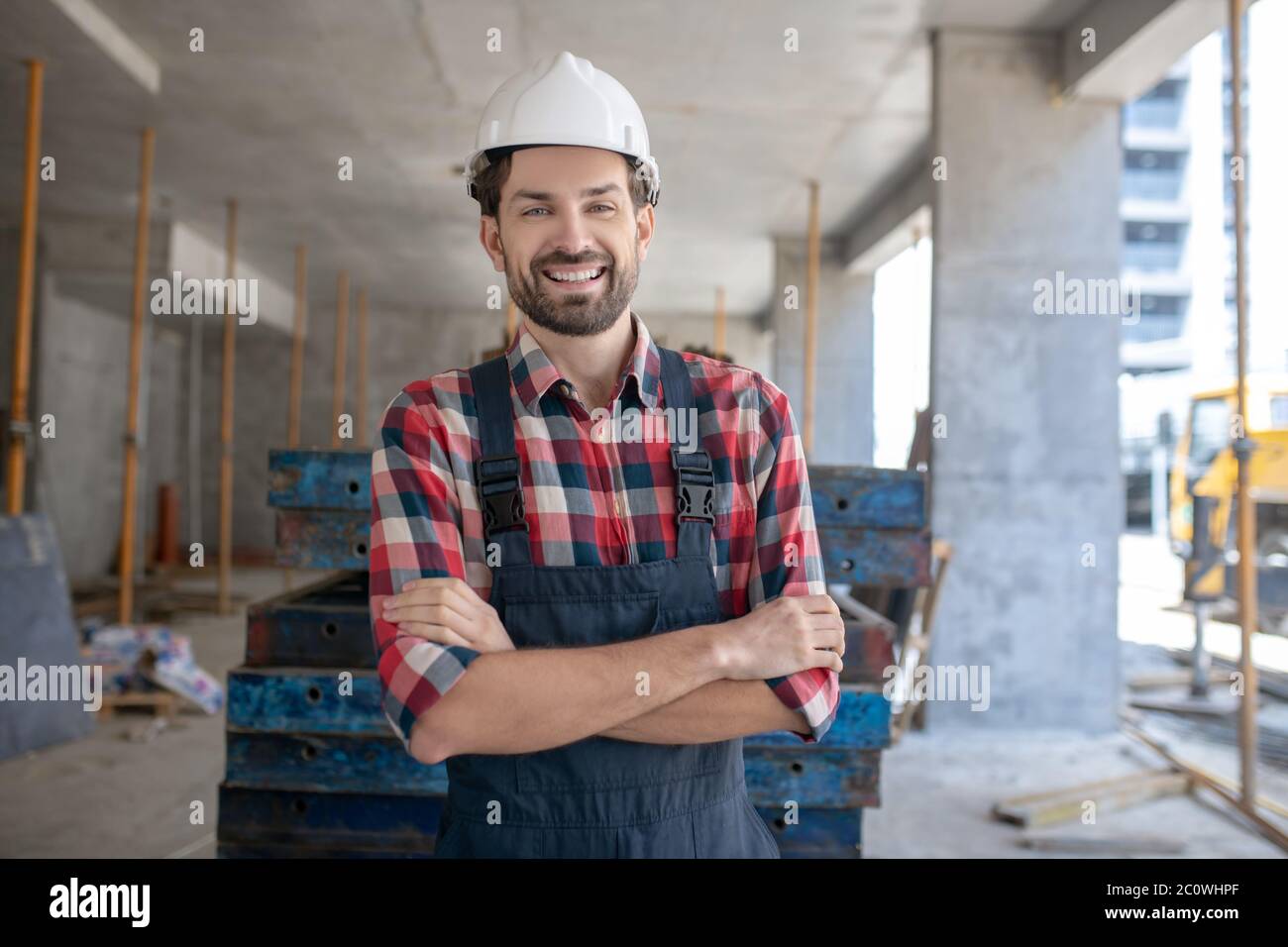 Bauarbeiter in Helm und kariertem Hemd stehend mit gefalteten Armen Stockfoto