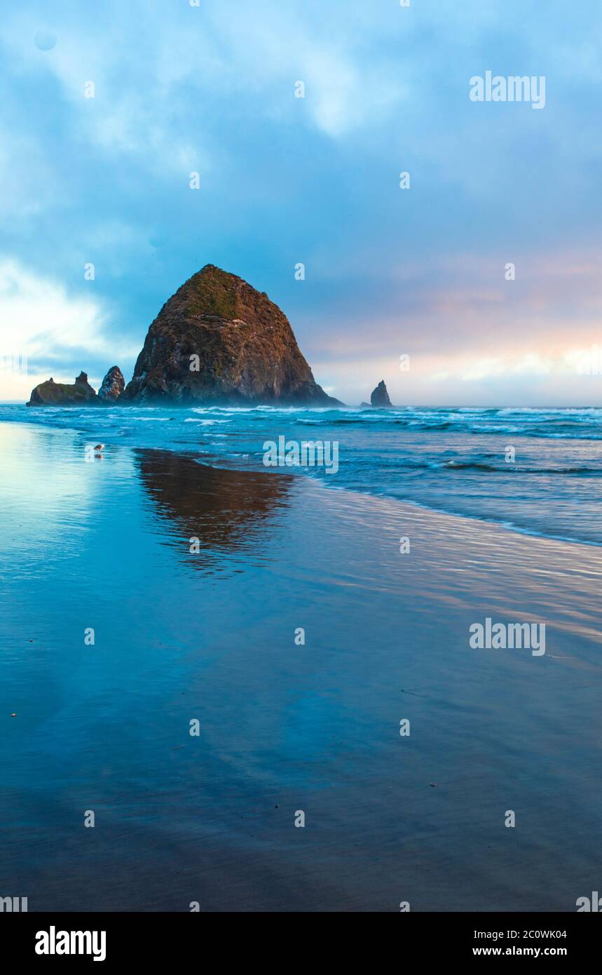 Vertikales Bild - riesiger Meeresstapel Haystack Rock, der sich im Wasser bei Sonnenuntergang am Cannon Beach in Oregon spiegelt Stockfoto