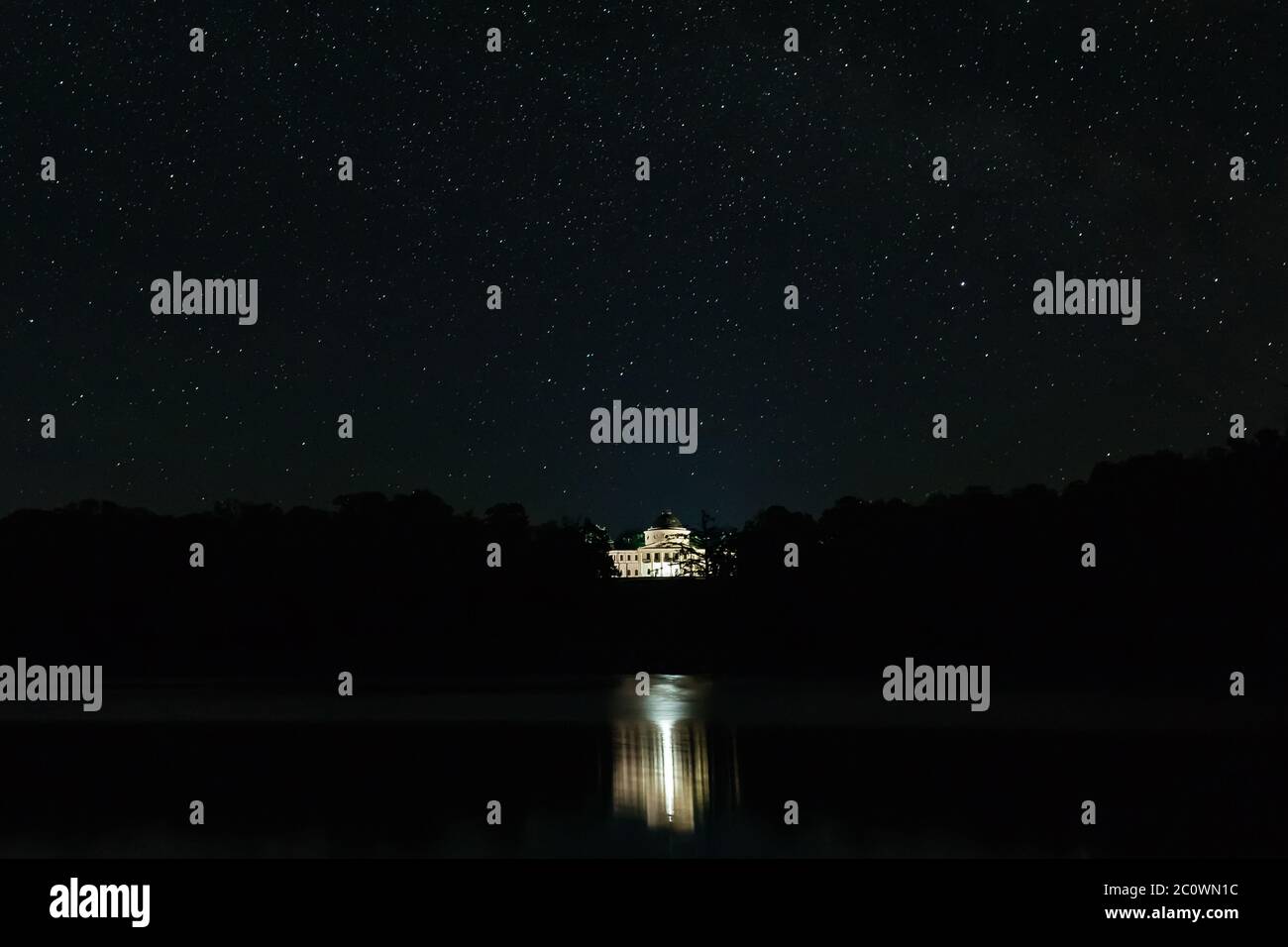 Weißer Palast unter den Bäumen, die sich im Wasser auf dem Hintergrund der sternenklaren Nacht spiegeln. Sternennacht Stockfoto