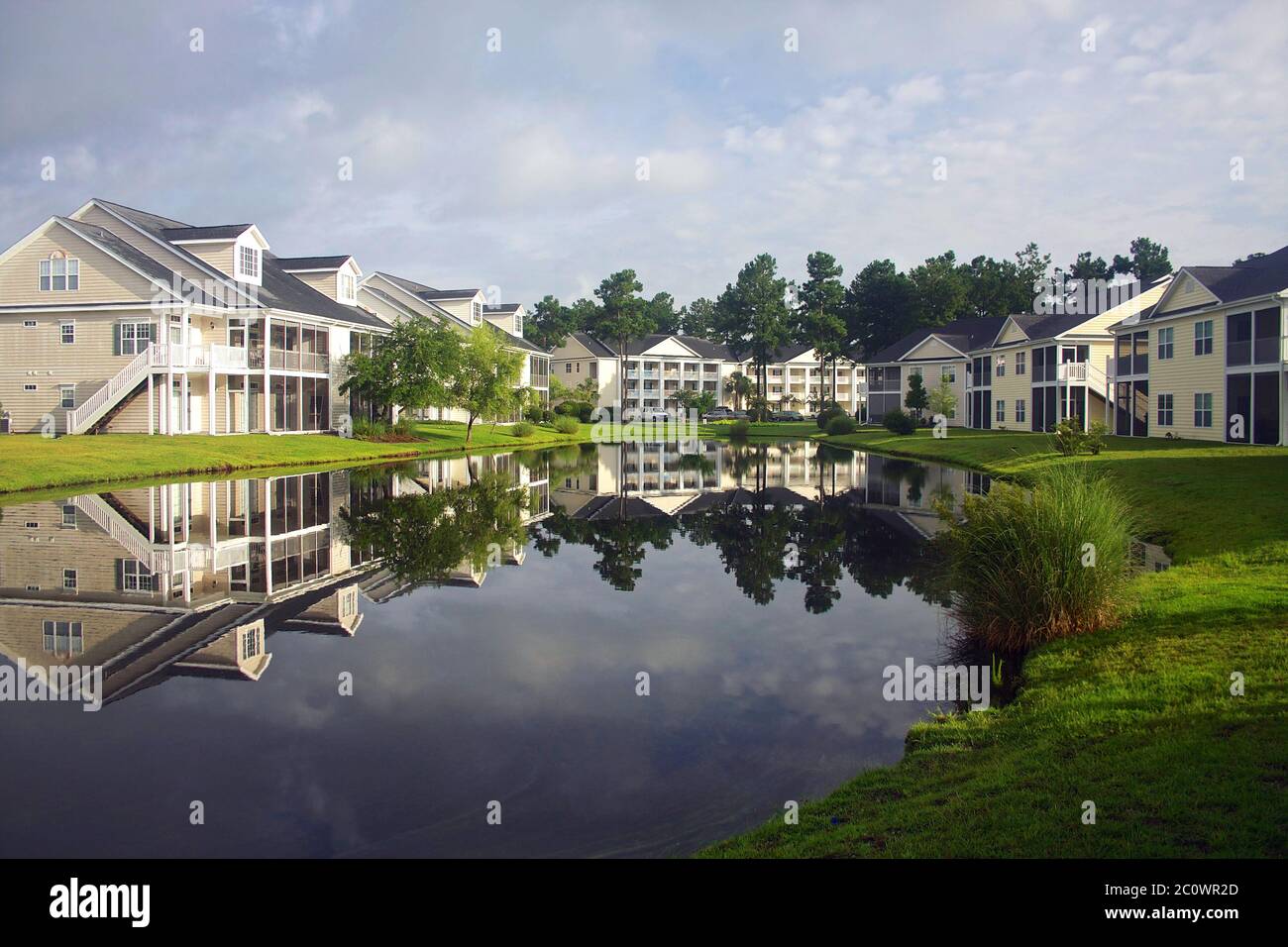 Hintergrund mit einem modernen Viertel mit Gebäuden rund um den Teich. Häuser und Bäume spiegeln sich im ruhigen Wasser während der schönen bewölkten Morgen Stockfoto