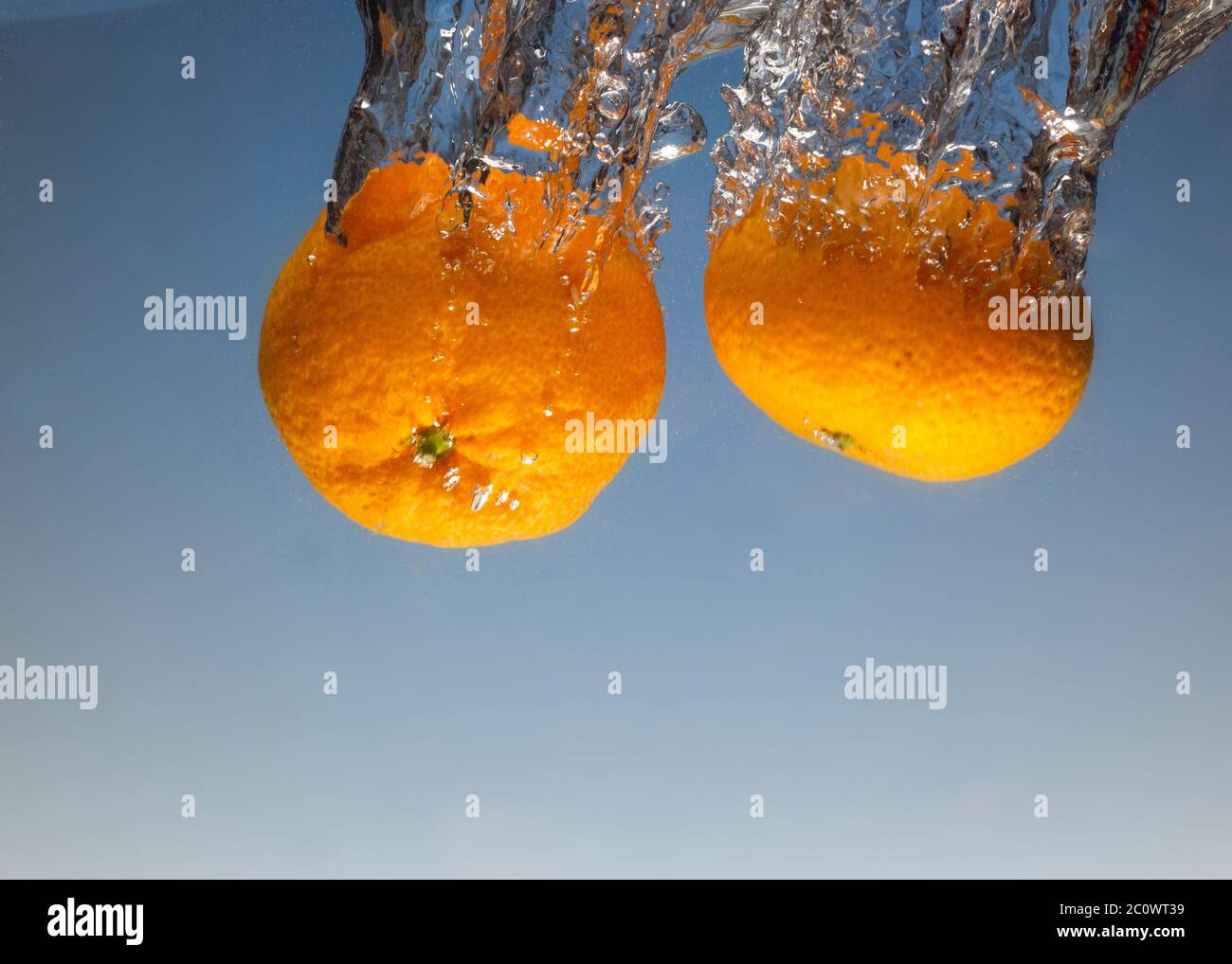 Reife Mandarine spritzt Wasser auf blauem Hintergrund Stockfoto