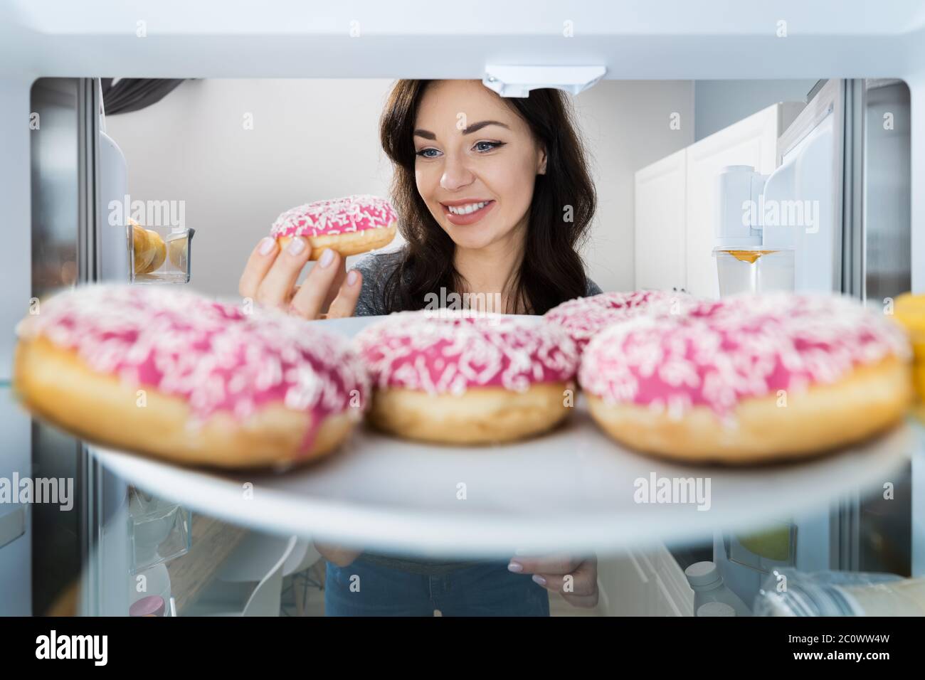 Happy Young Woman Einnahme Donut Aus Kühlschrank Oder Gefrierschrank Stockfoto