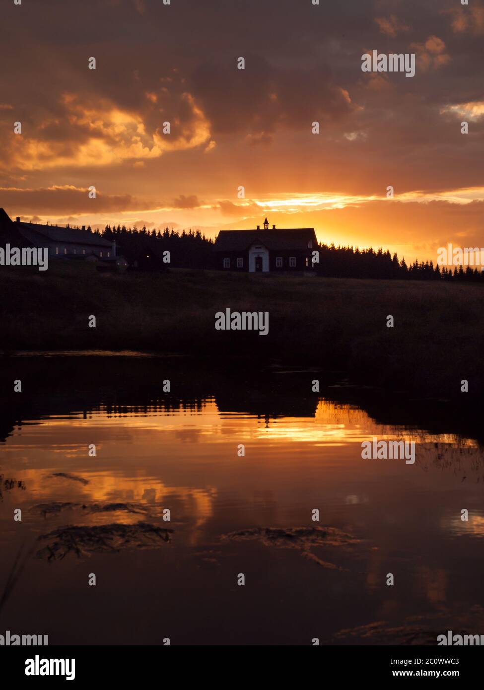 Sonnenuntergang am Berg mit Flussspiegelung und dunkler Silhouette von Wald und Dach, Jizerka Dorf, Isergebirge, Tschechische Republik Stockfoto