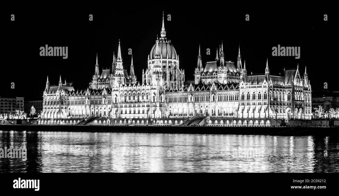 Nachtansicht des beleuchteten historischen Gebäudes des ungarischen Parlaments, aka Orszaghaz, mit typischer symmetrischer Architektur und zentraler Kuppel auf dem Donauufer in Budapest, Ungarn, Europa. Es ist ein bemerkenswertes Wahrzeichen und Sitz der Nationalversammlung von Ungarn. Schwarzweiß-Bild. Stockfoto