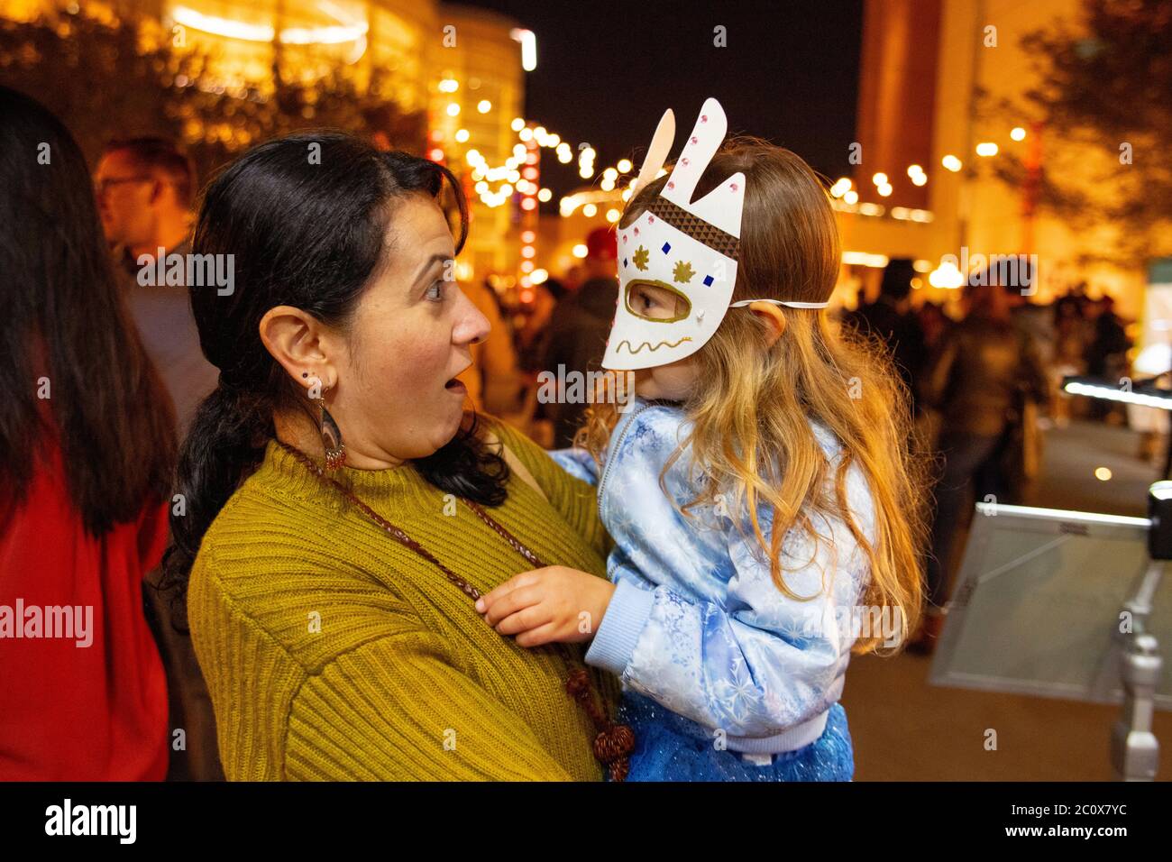 Eine hispanische Mutter gibt der festlichen Gesichtsmaske ihrer Tochter bei einer Mardi Gras Observation in Costa Mesa, CA, einen überraschenden Ausdruck. Stockfoto