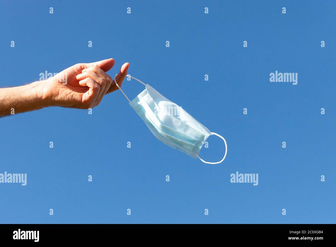 Der Mensch zieht die medizinische Schutzmaske aus und hält sie auf dem blauen Himmel auf dem Finger, genießt das Leben, saubere frische Luft nach der Covid-19 Pandemie, sich selbst zu sein Stockfoto