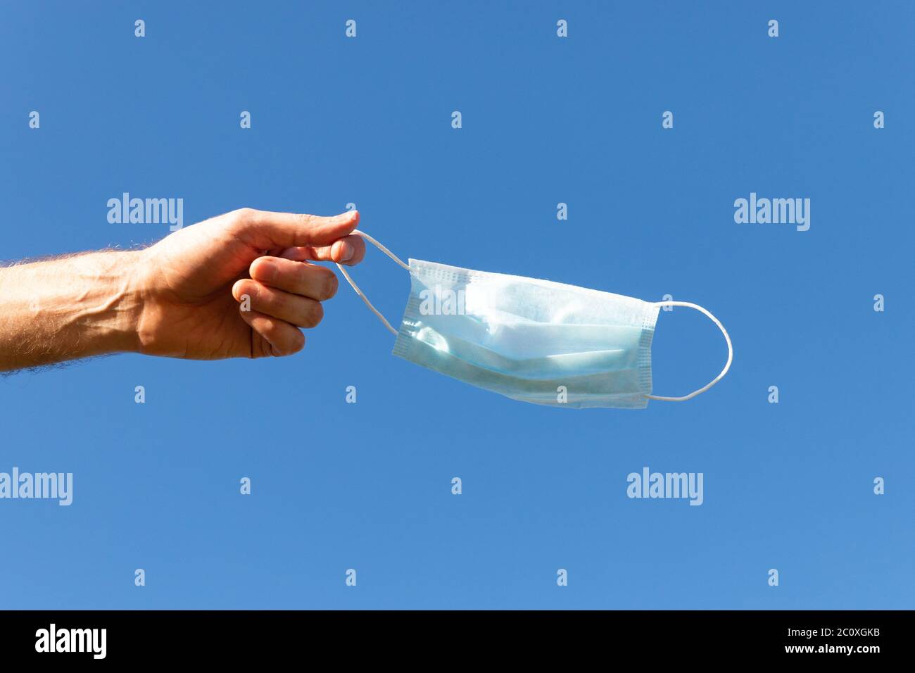 Der Mensch zieht die medizinische Schutzmaske aus und hält sie auf dem blauen Himmel auf dem Finger, genießt das Leben, saubere frische Luft nach der Covid-19 Pandemie, sich selbst zu sein Stockfoto