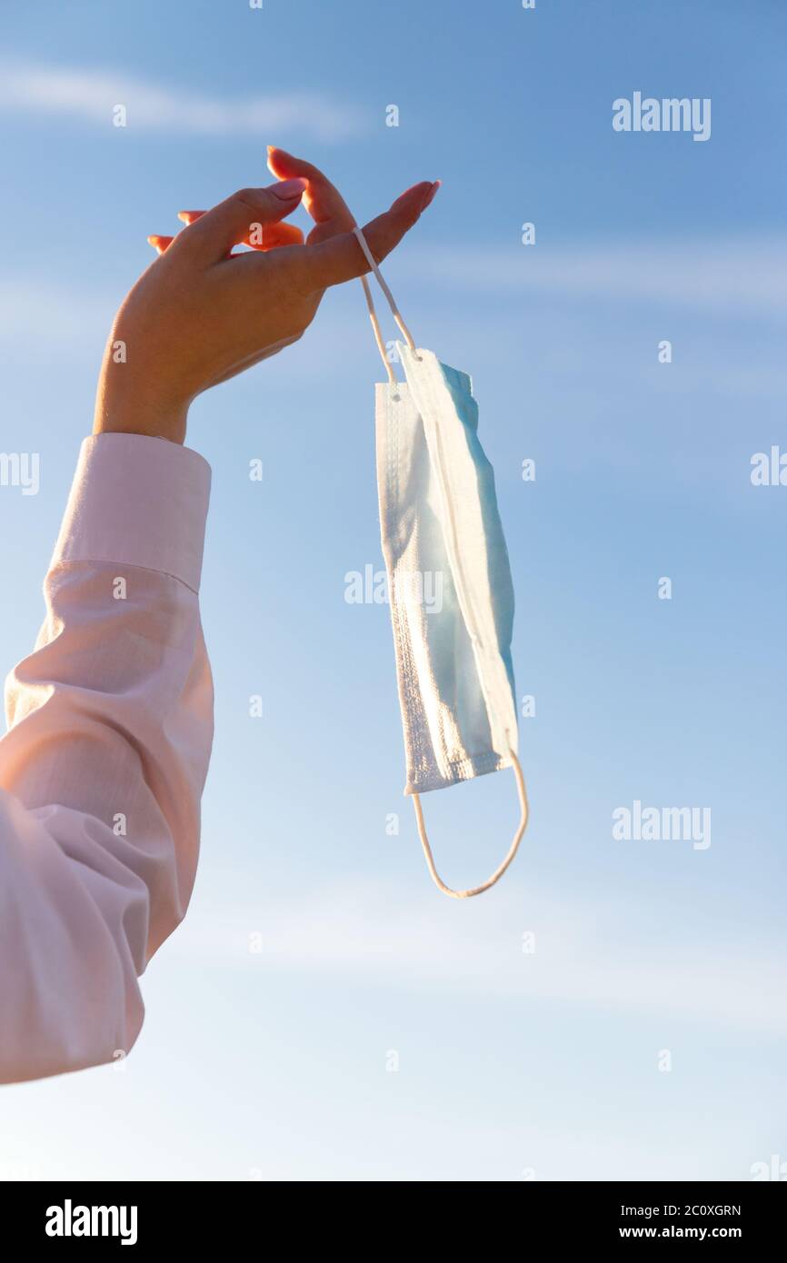 Glückliche Frau zieht medizinische Schutzmaske hält es auf ihrem Finger auf blauem Himmel Hintergrund, genießt das Leben, saubere frische Luft nach Covid-19 Pandemie, sel Stockfoto