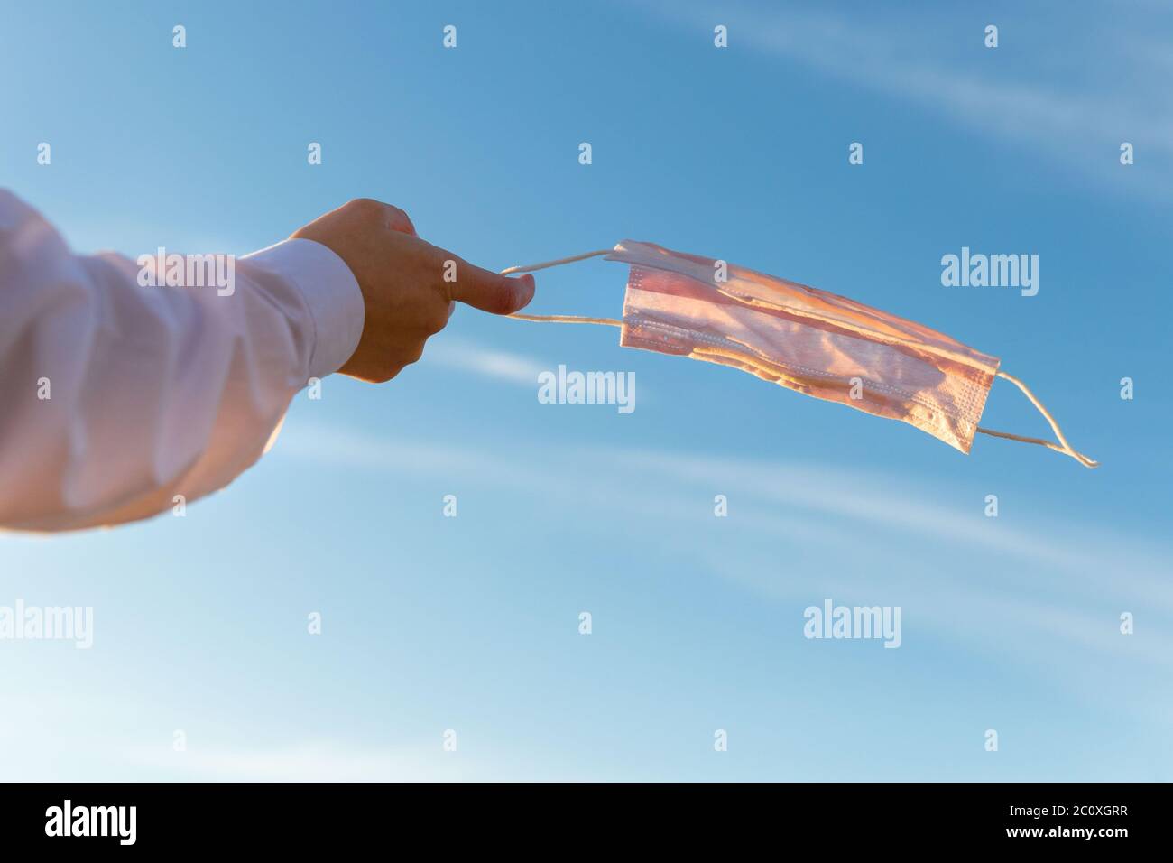 Frau zieht medizinische Schutzmaske aus und hält sie auf ihrem Finger auf blauem Himmel Hintergrund, genießt das Leben, saubere frische Luft nach Covid-19 Pandemie, selbst- Stockfoto