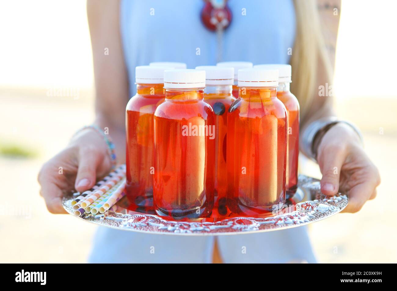 Glückliche junge Frau hält ein Gericht mit einem Getränk bei Sonnenuntergang Party Stockfoto