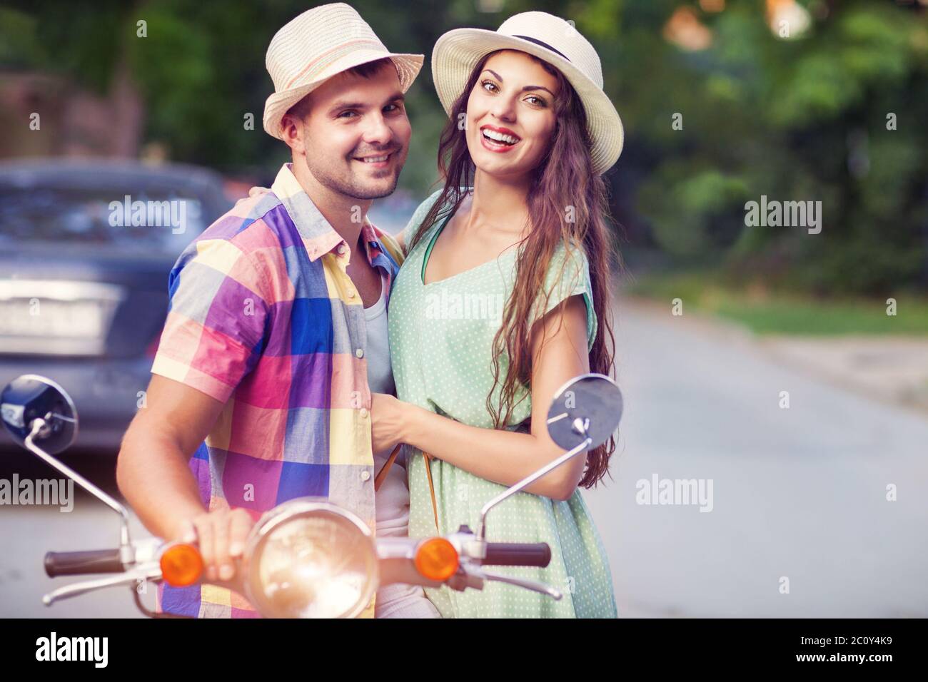 Glückliches junges Paar von einem alten Roller in der Straße trägt Hüte Stockfoto