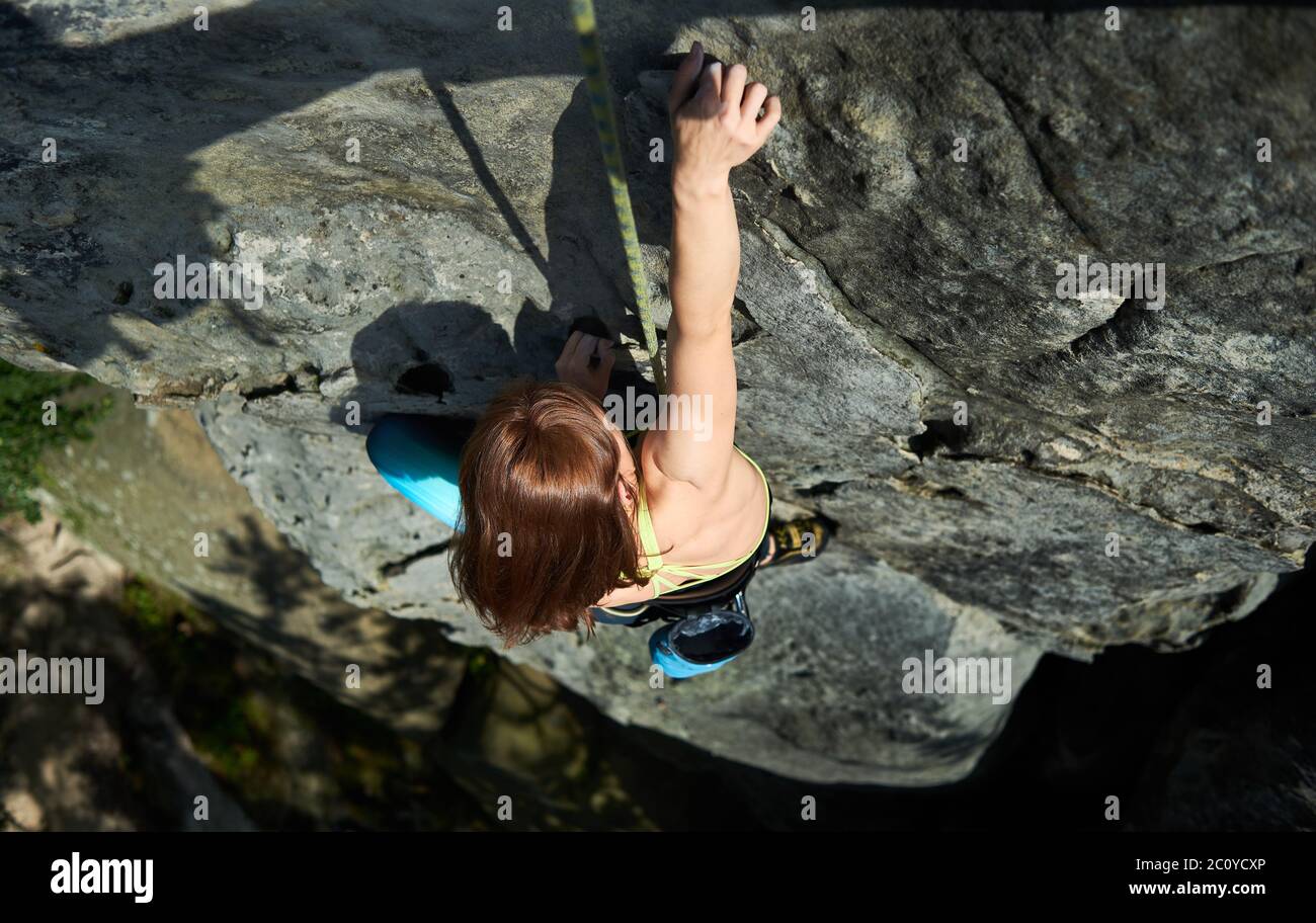 Horizontale Momentaufnahme der hübschen Frau im Sicherheitsgeschirr, Klettern den Felsen mit Seil, machen nächsten Schritt mit einer Hand helfen. Draufsicht. Konzept des Bergsports, Klettern Stockfoto