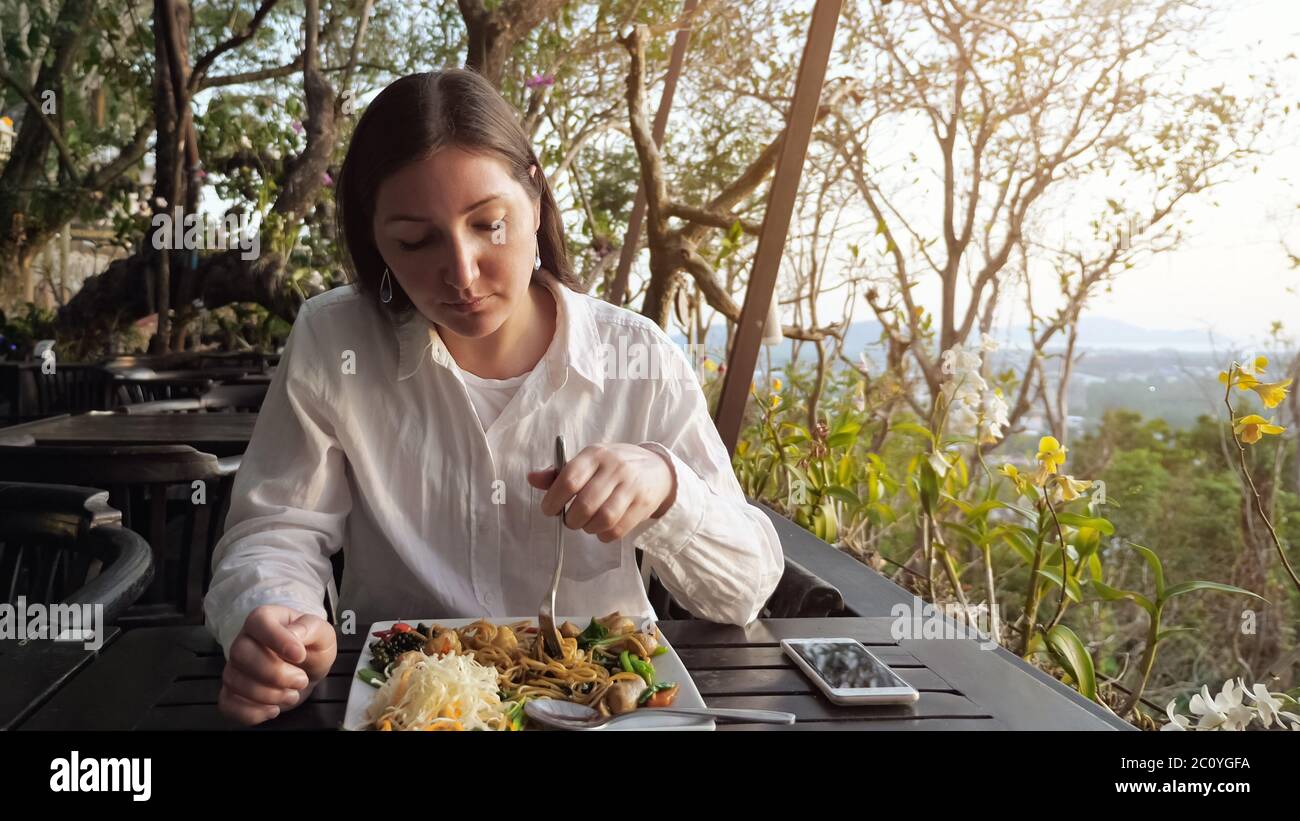 Brunette Frau hat Abendessen Nudeln mit Gemüse in einem Café auf dem Hügel. Stockfoto