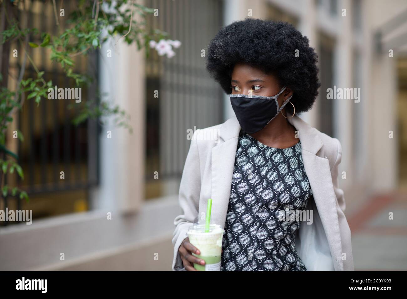 Modische dunkelhäutige Mädchen zu Fuß in der Stadt trägt schützende Stoff Gesichtsmaske in Coronavirus Pandemie, COVID-19. Stockfoto