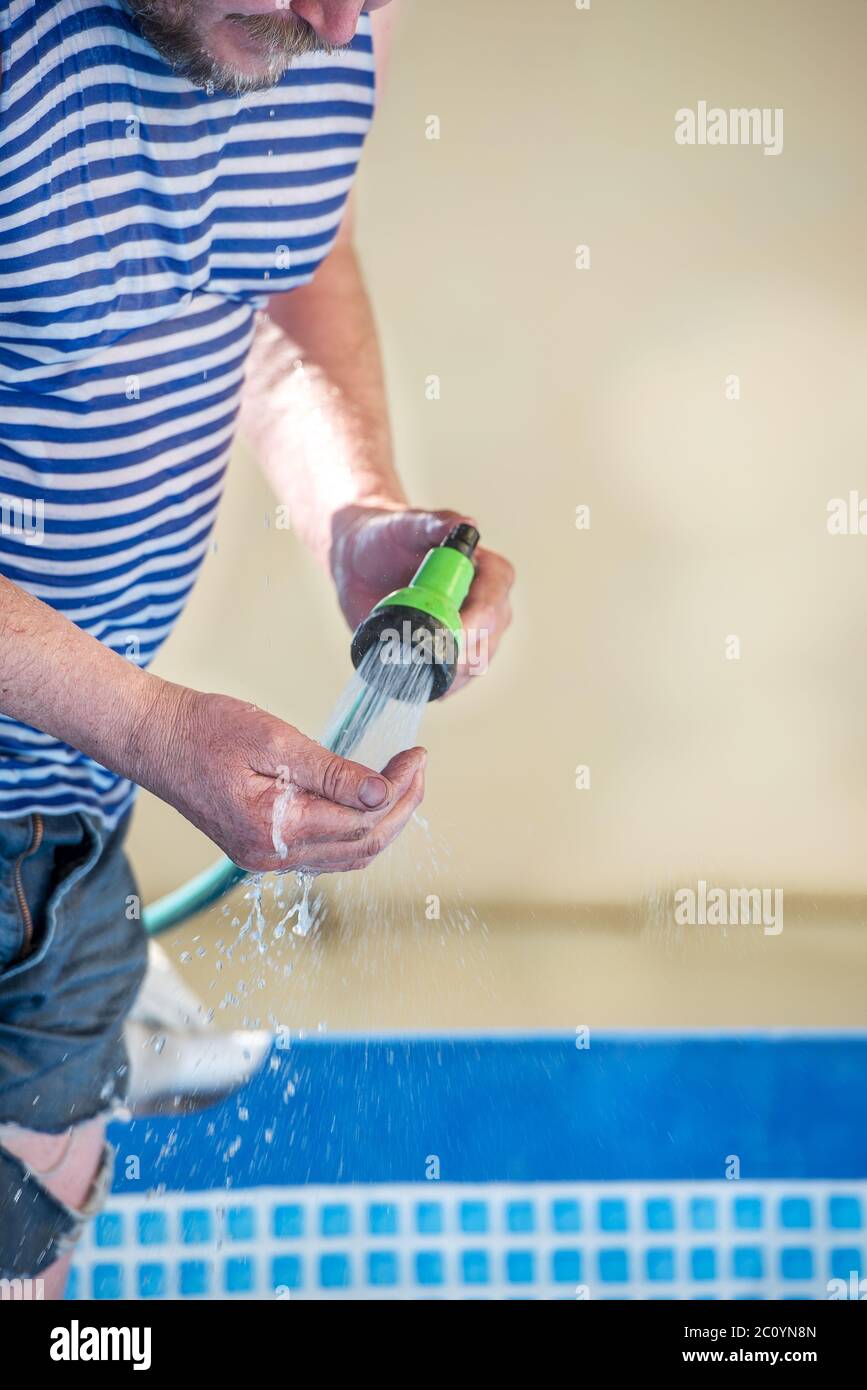 Mann gießt Wasser aus einem Schlauch in den Pool an einem heißen Tag Stockfoto