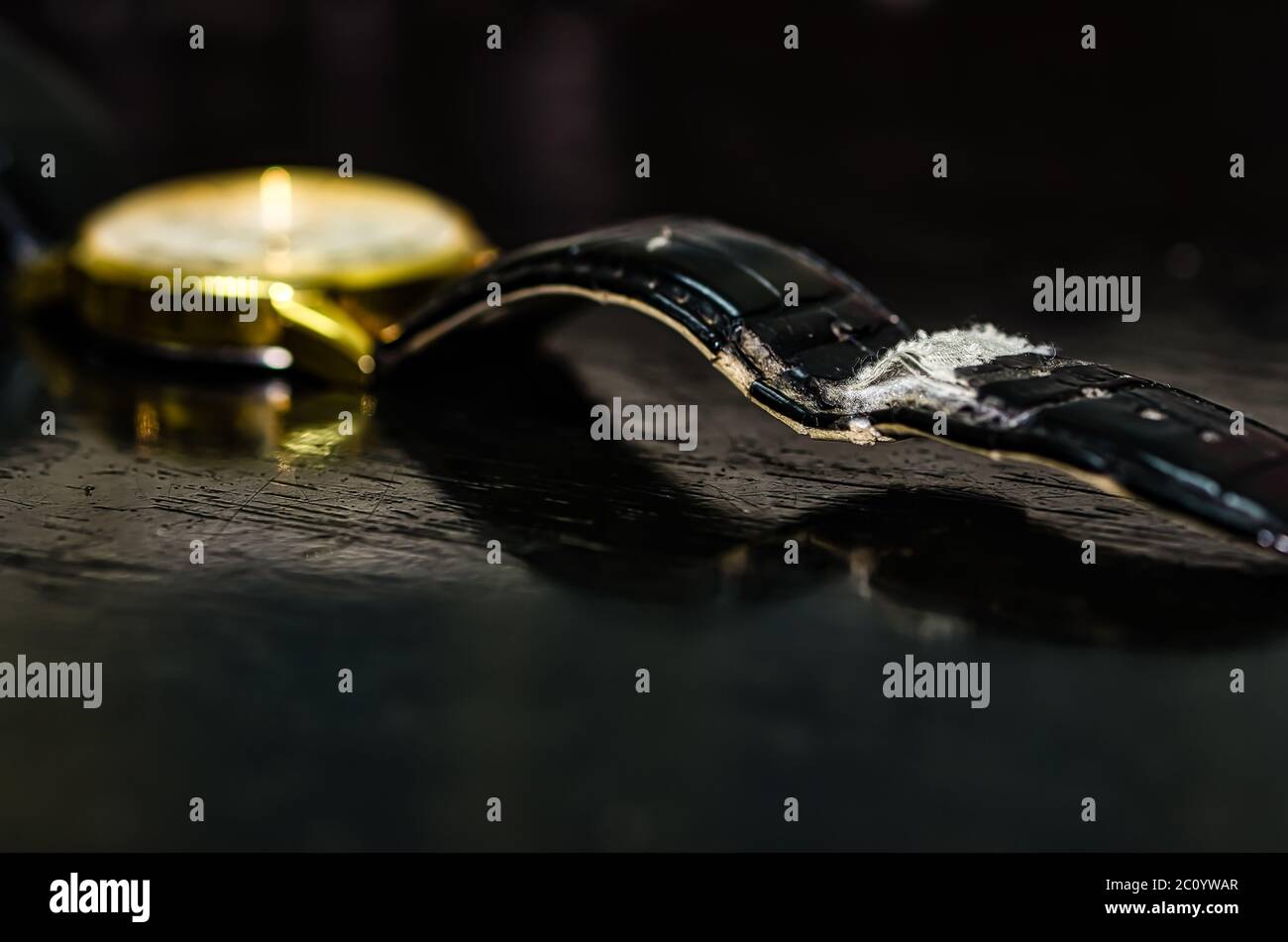Gebrauchter und abgenutzter schwarzer Gürtel einer goldenen Uhr auf einem abgenutzten schwarzen Tisch. Stockfoto