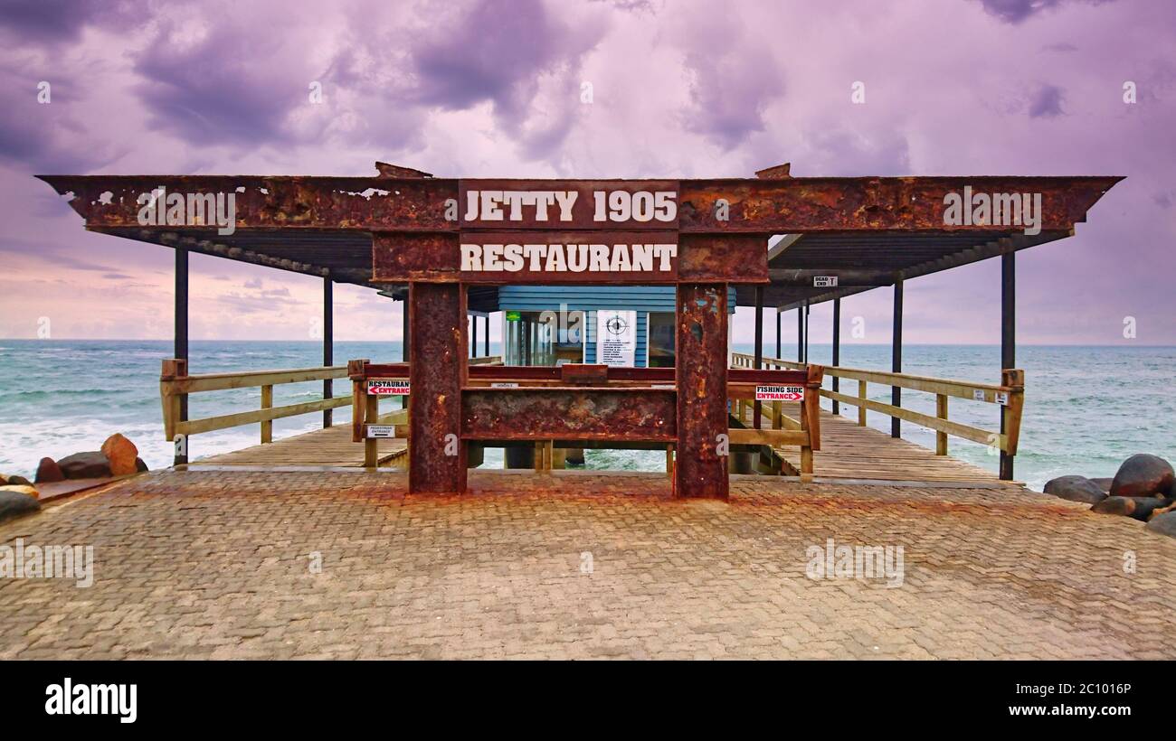 Swakopmund, Namibia - 25. Nov 2015: Rostiger Stahleingang zum Jetty 1905 Restaurant und Pier an der Küste von Swakopmund. Dunkler, wolkig stürmischer Himmel Stockfoto