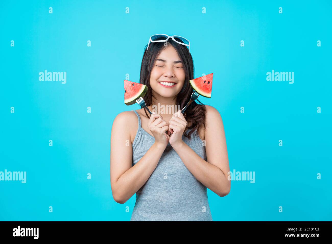 Portrait Attraktive asiatische junge Frau hält zwei Stück Folie von Wassermelone und trägt Mode Sonnenbrille auf isolierten blauen Hintergrund, kopieren Spa Stockfoto