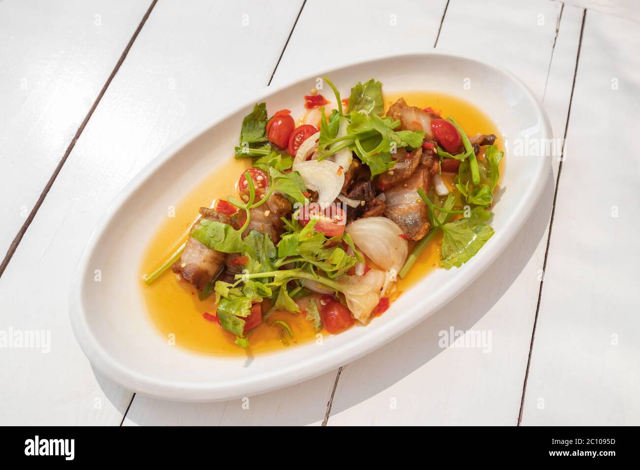 Knuspriger Schweinebauch würziger Salat auf weißem Teller und weißem Holztisch Stockfoto